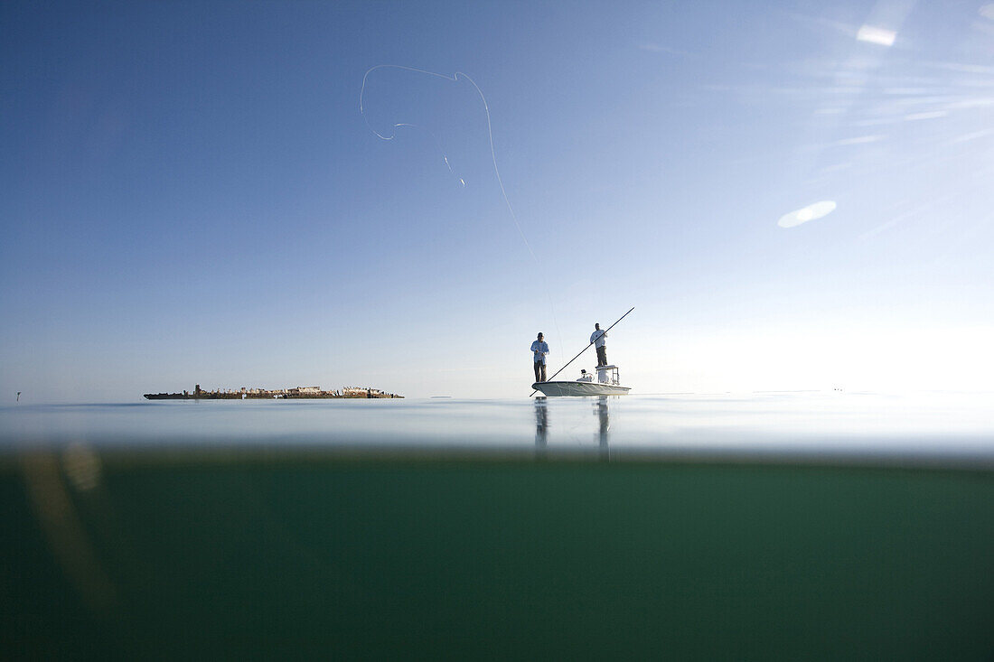 Over and Underwater View of Two Men Fly Fishing in Boat Near Shipwreck, Florida Keys, USA