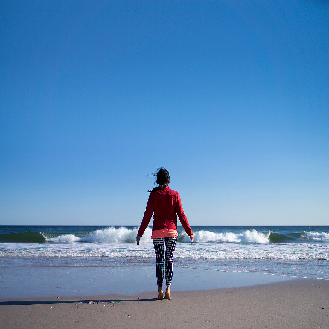 Woman in Casual Clothes Standing on Tiptoes on Beach, Rear View