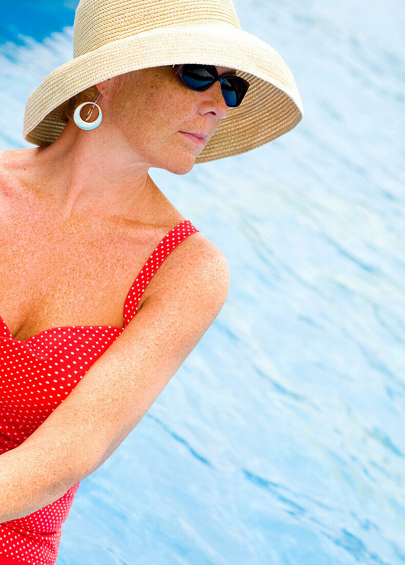 Frau am Pool mit Sonnenbrille und Sonnenhut