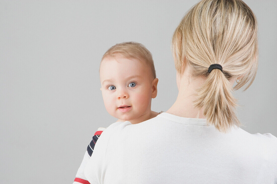 A Toddler Boy Looking Over His Mother's Shoulder