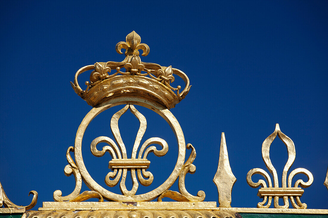 'Gold Crown And Fleur-De-Lis On The Grand Trianon Gates Against A Blue Sky In The Gardens Of The Palace Of Versailles; Paris, France'