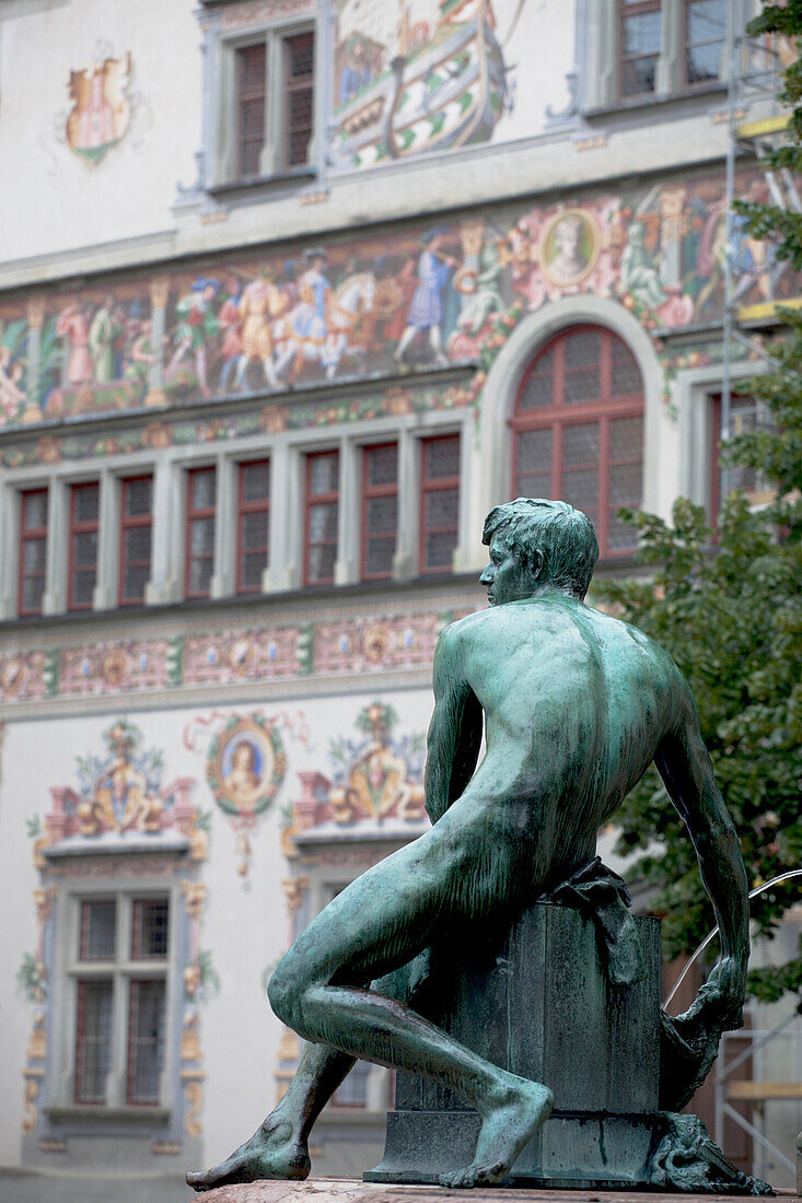 'Bronze Male Statue With Colorfully Painted Buildings In The Background; Lindau, Germany'