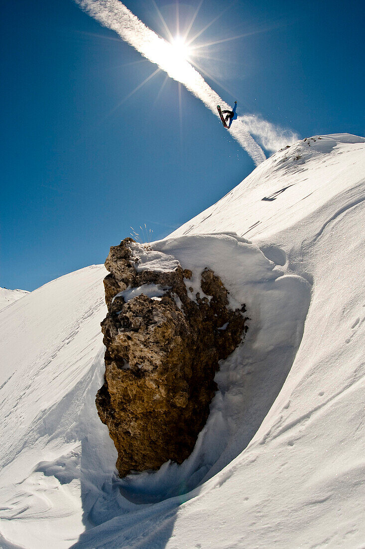 France, Tignes, Savoie, snowboarder jumping behind a rock