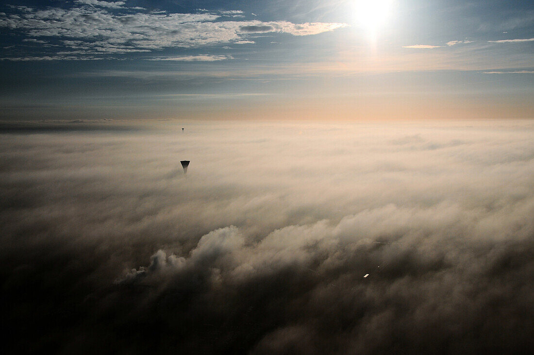 Aerial view above the fog. Wide Shot. Two water towers and second background. Morning light against the light