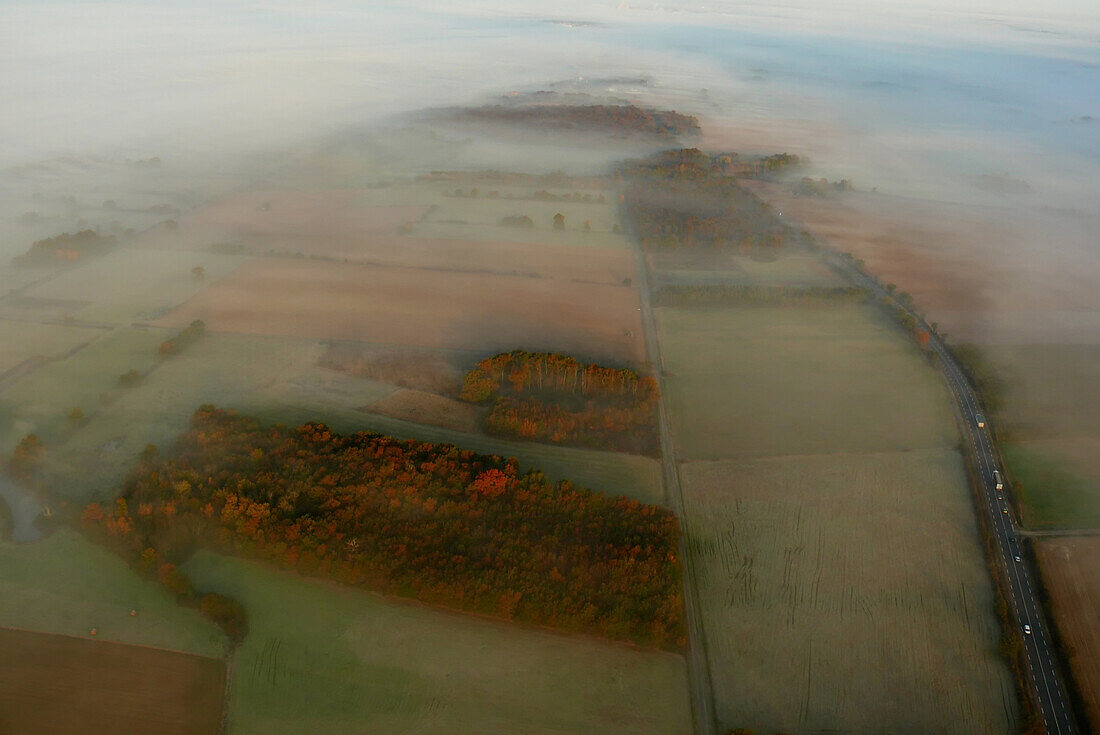 Aerial view above the fog. Campaign, groves of trees in the foreground with grazing light and autumn colors. Road on the right