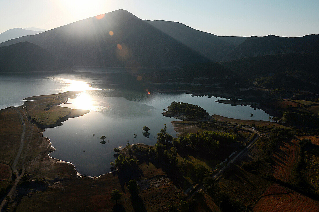Aerial view of a lake against the light. Field and trees in the foreground. Mountain in the background