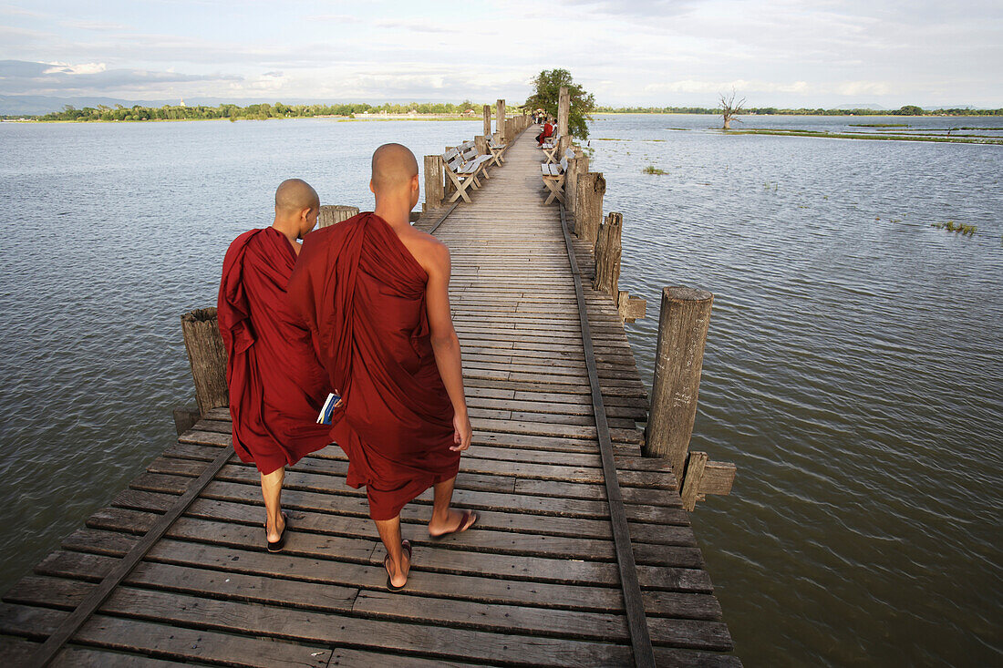 'Buddhist monks walk across U Bein Bridge, made of Teak wood; Mandaly, Burma'