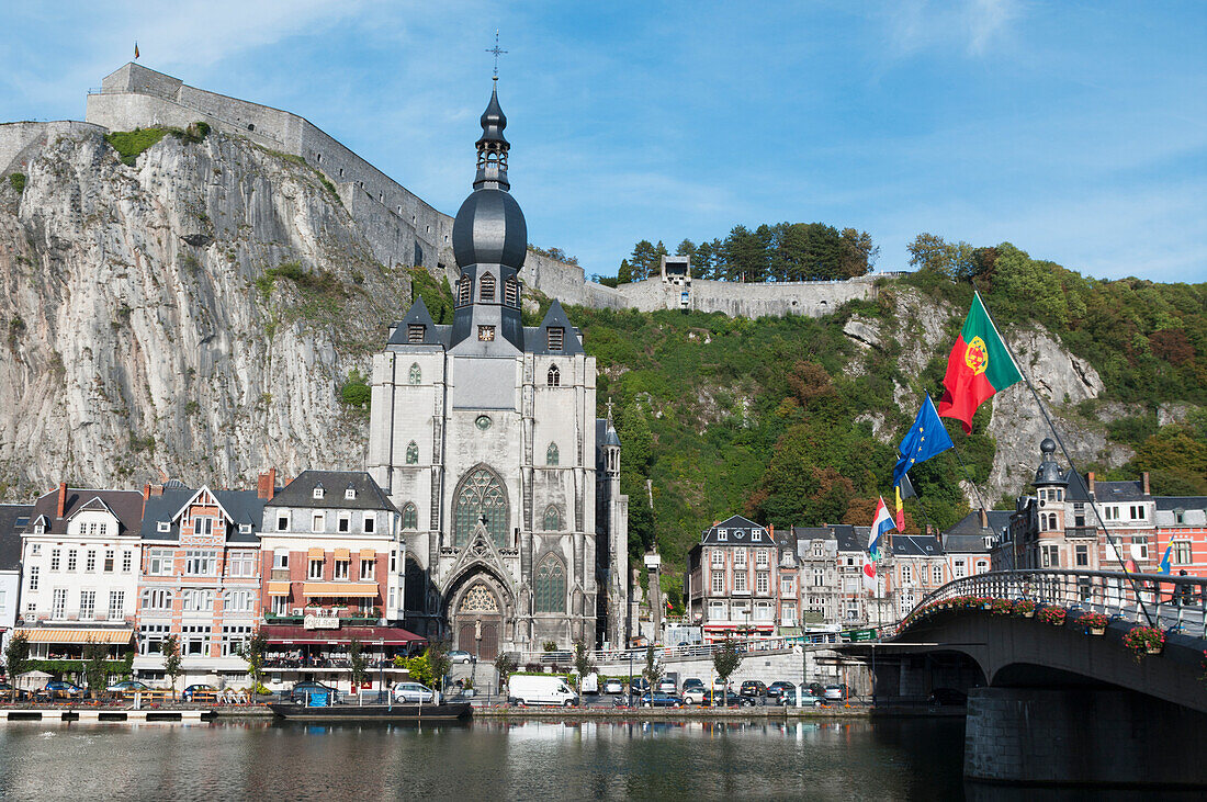 'A church and other buildings along the water and flags flying; Dinant, Belgium'