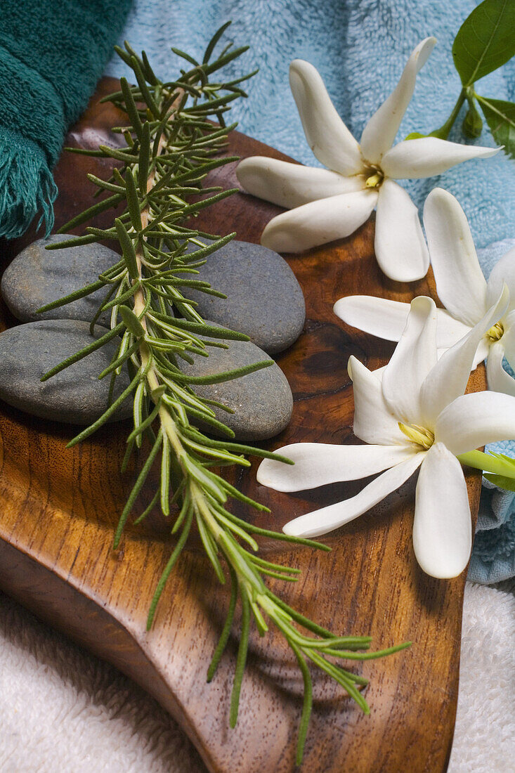 Spa Elements, Flowers, Grey Stones And A Sprig Of Rosemary Ona Wooden Platter With Towels Surrounding.