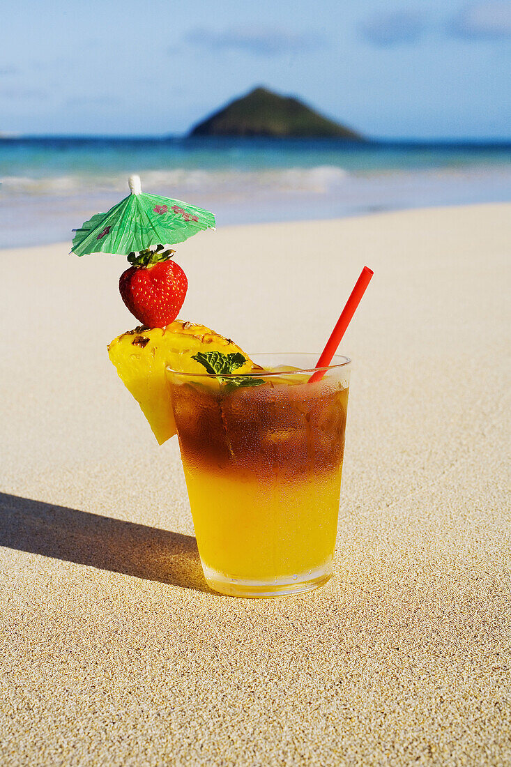 A Mai Tai Garnished With Pinapple And A Strawberry, Sitting In The Sand On The Beach.