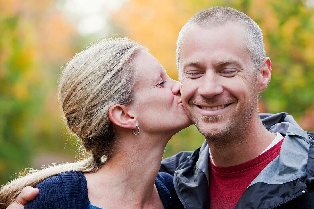 'Wife Kissing Husband On The Cheek In A Park In Autumn; Edmonton, Alberta, Canada'