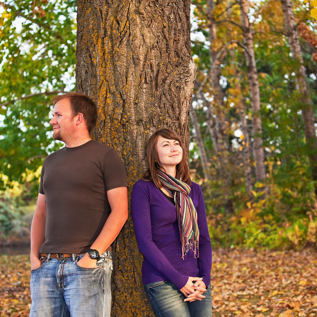 'Young married couple leaning against a tree in a park in autumn;Edmonton alberta canada'