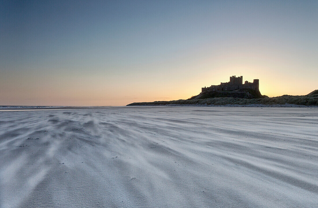 'Sand Blowing Across The Beach With Bamburgh Castle In The Distance At Sunset; Bamburgh, Northumberland, England'