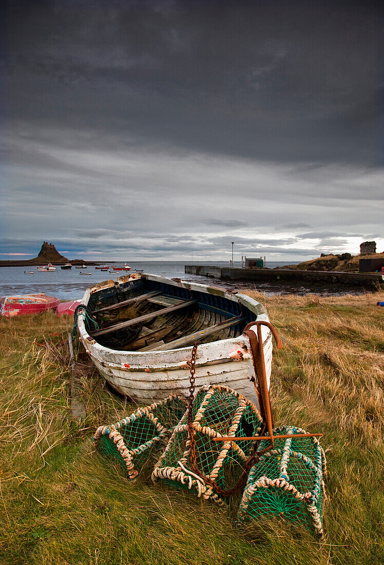 'A Weathered Boat And Fishing Equipment Sitting On The Shore With Lindisfarne Castle In The Distance; Lindisfarne, Northumberland, England'