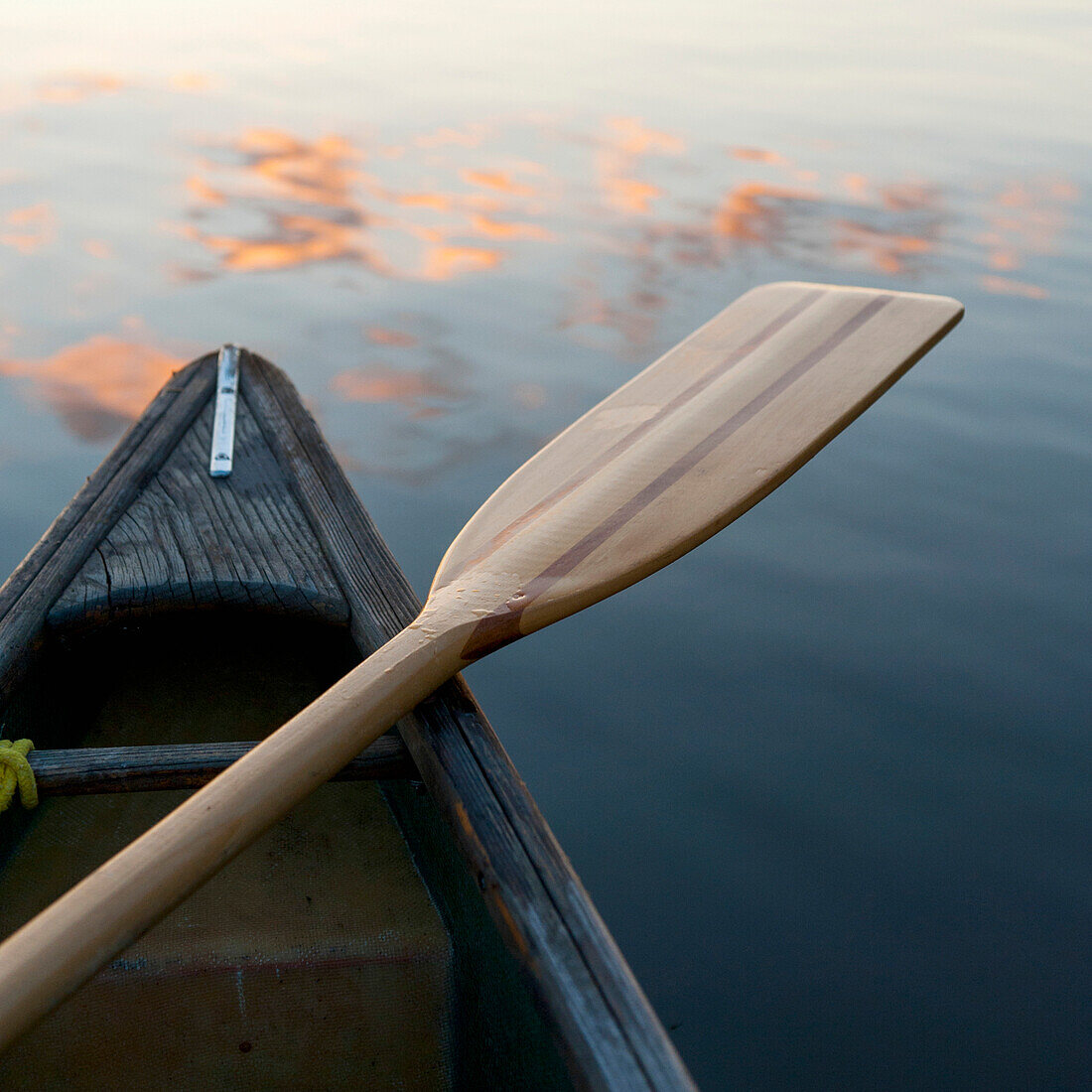 'A Boat And Paddle Sit On A Tranquil Lake With Clouds Reflected In The Water; Lake Of The Woods, Ontario, Canada'