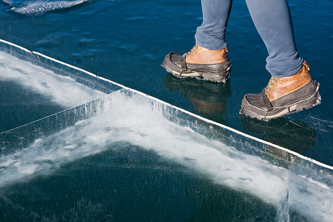 'Close Up Of The Boots Of A Female Walking On A Frozen Mountain Lake With Ice Cracks; Alberta, Canada'