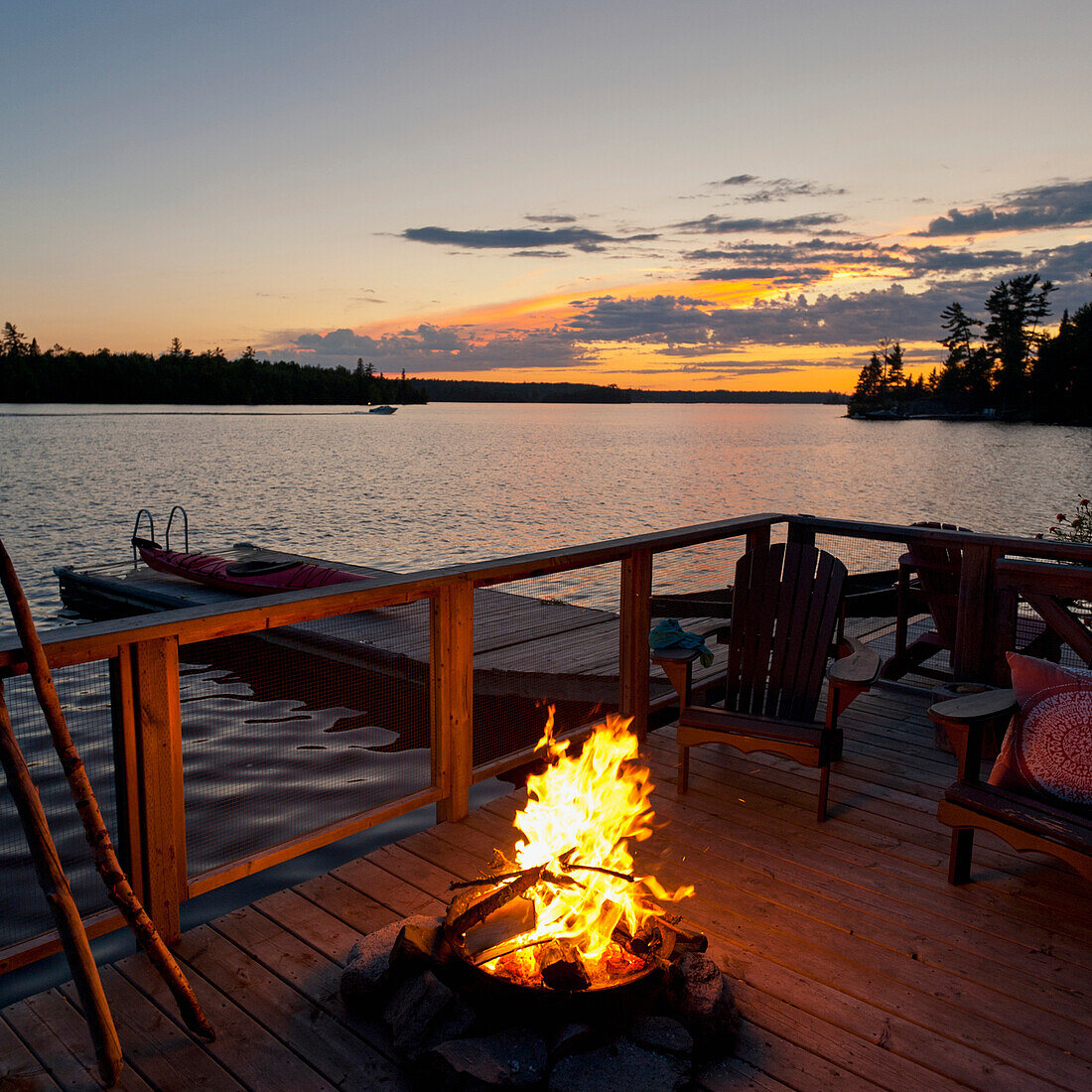 'Burning Fire On A Wooden Dock Along The Water's Edge At Sunset; Lake Of The Woods, Ontario, Canada'