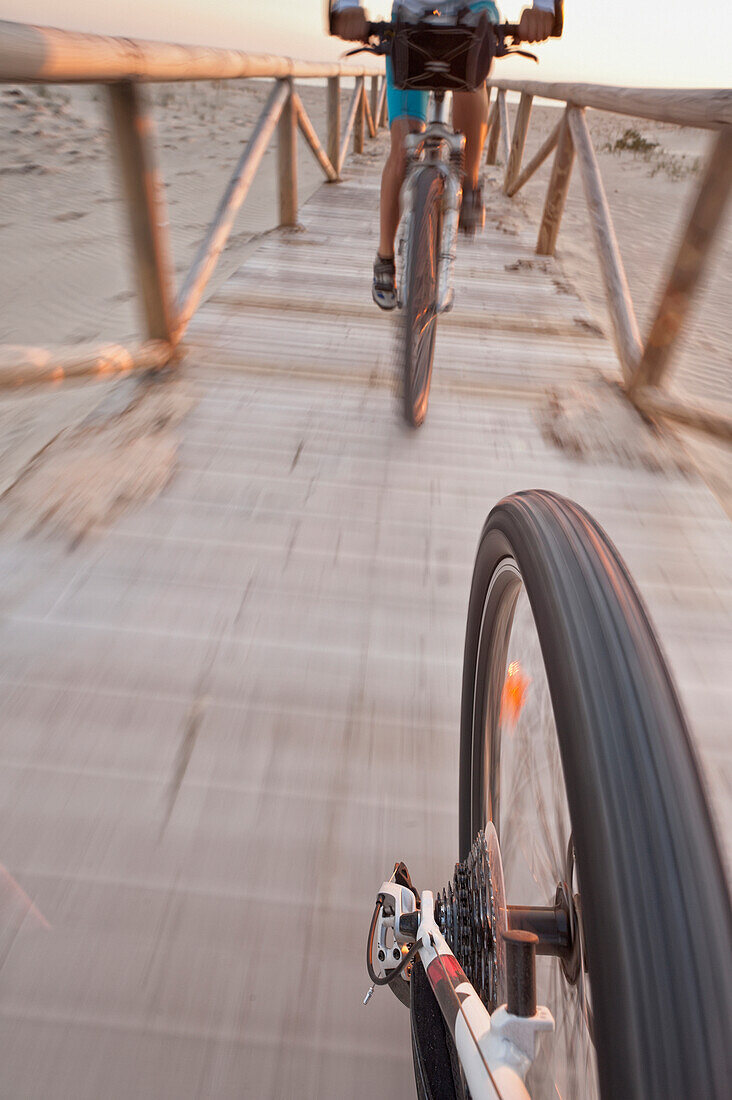 'Cyclists Ride Down A Wooden Boardwalk On The Beach; Tarifa, Cadiz, Andalusia, Spain'