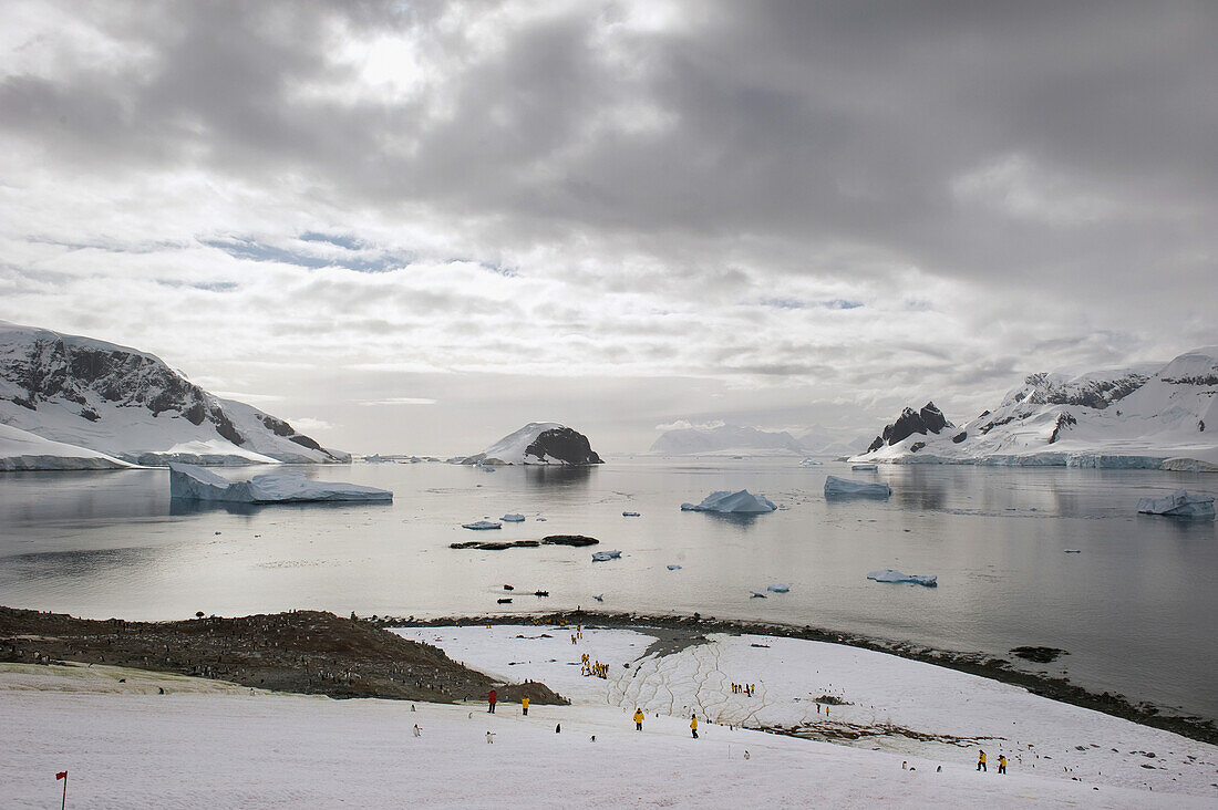 'People Standing On The Ice With Icebergs And Mountains Along The Coastline; Antarctica'