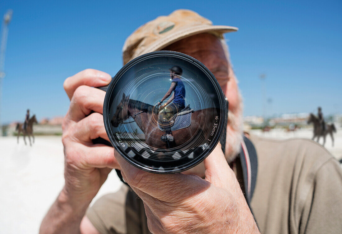 'A man holds a camera with a reflection of a young woman sitting on a horse in the lens;Mijas malaga andalusia spain'