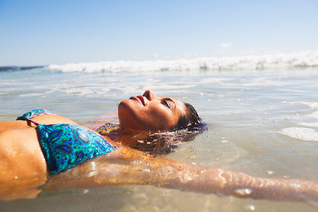 'A young woman lays in the shallow water off the beach;Gold coast queensland australia'