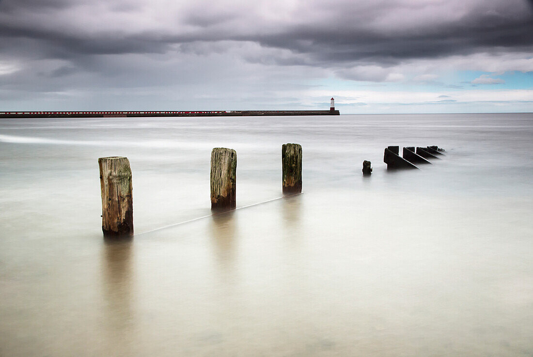 Wooden posts in the ocean with a lighthouse at the end of a pier