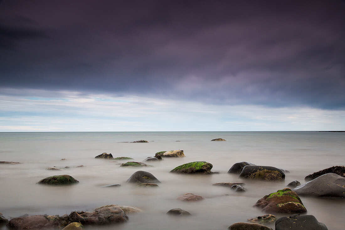 'Rocks in tranquil water under storm clouds;Northumberland england'