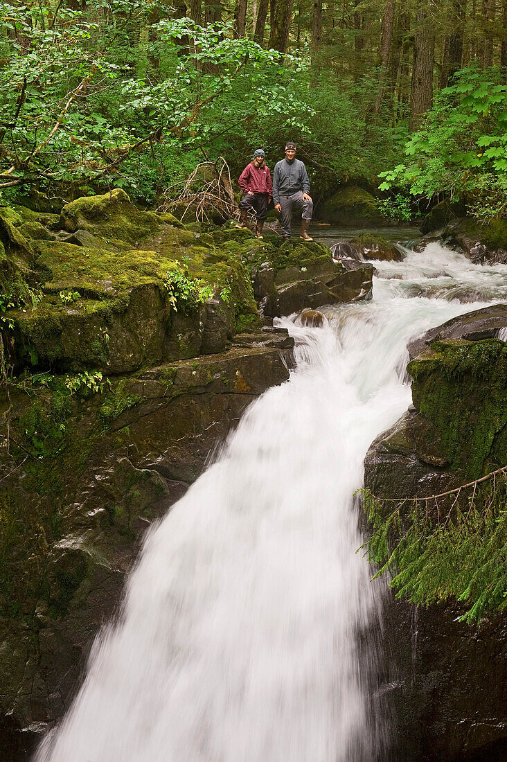 Two Hikers Stand At The Top Of Sawmill Creek Falls In The Tongass National Rainforest Near Juneau, Southeast Alaska