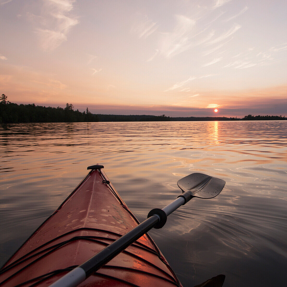 'Bow of a red kayak and paddle on a tranquil lake at sunset;Keewatin ontario canada'