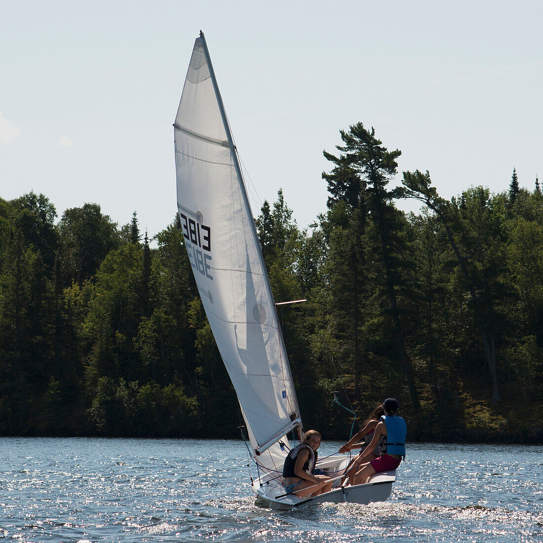 'Three teenagers on a sailboat in a lake;Kenora ontario canada'