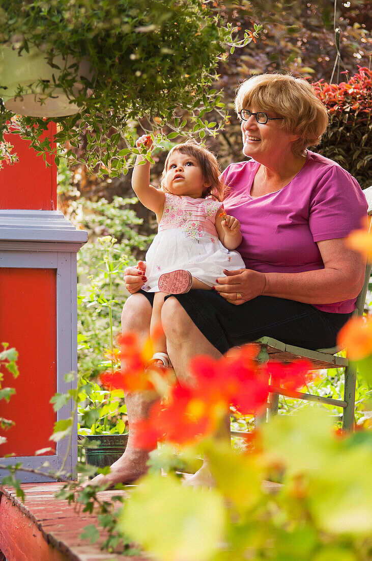 'Grandmother And Child Sitting On Front Porch With Many Plants Surrounding Them; Winnipeg Manitoba Canada'