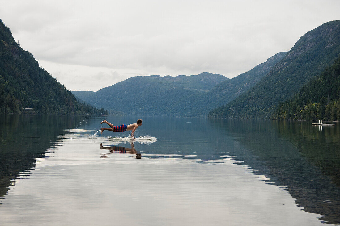 'A Young Man Leaps Onto His Body Board In Cameron Lake; British Columbia Canada'