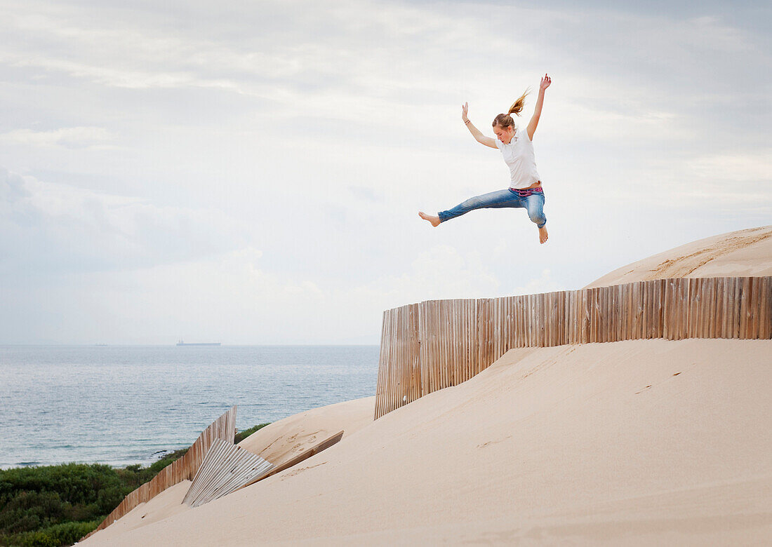 'A Woman Jumps Over A Fence In The Punta Paloma Sand Dunes; Tarifa, Cadiz, Andalusia, Spain'
