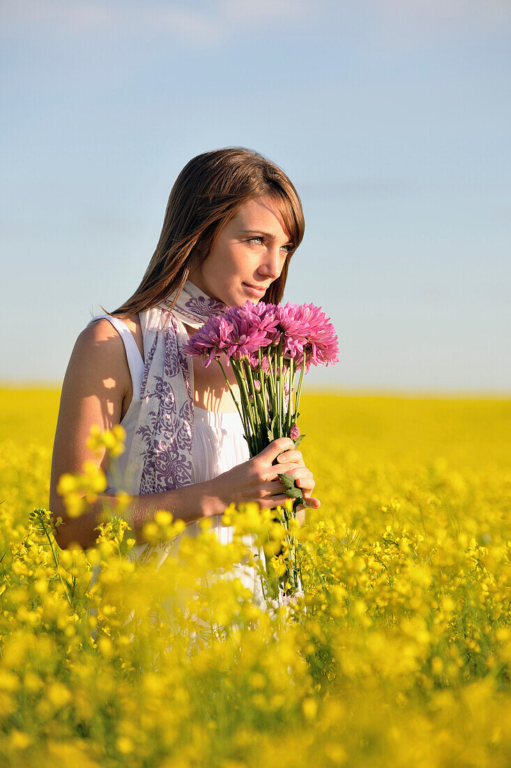 Woman Sniffing Purple Flowers While Standing In Golden Field
