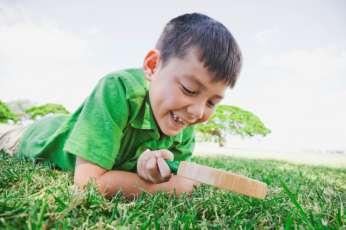 'A boy looking through a magnifying glass at the grass; Honolulu, Oahu, Hawaii, United States of America'