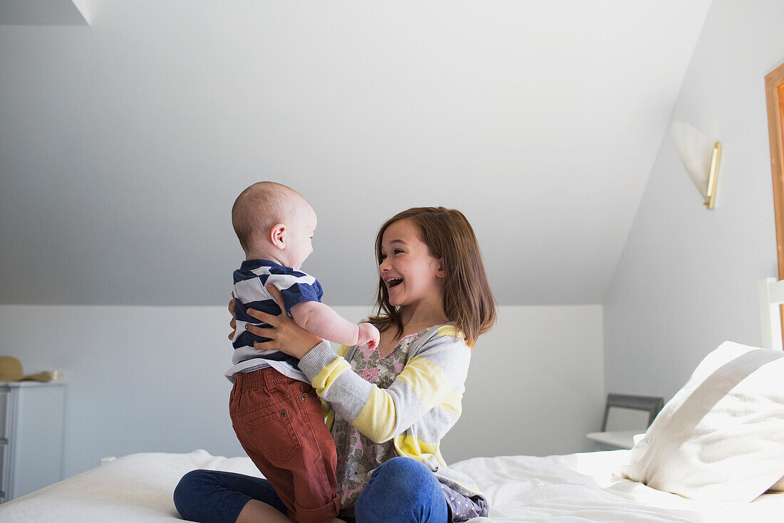 'A sister playing with her baby brother on a bed at home; Victoria, British Columbia, Canada'