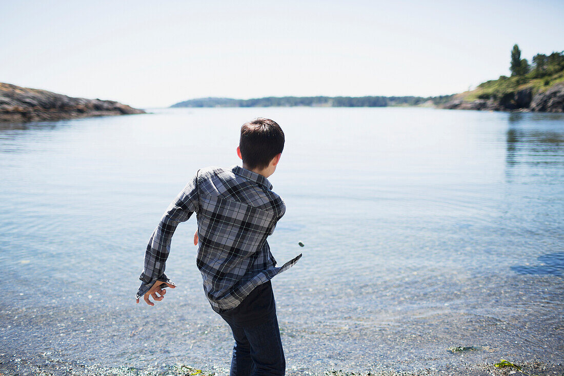 'A boy throws rocks into the water; Victoria, British Columbia, Canada'