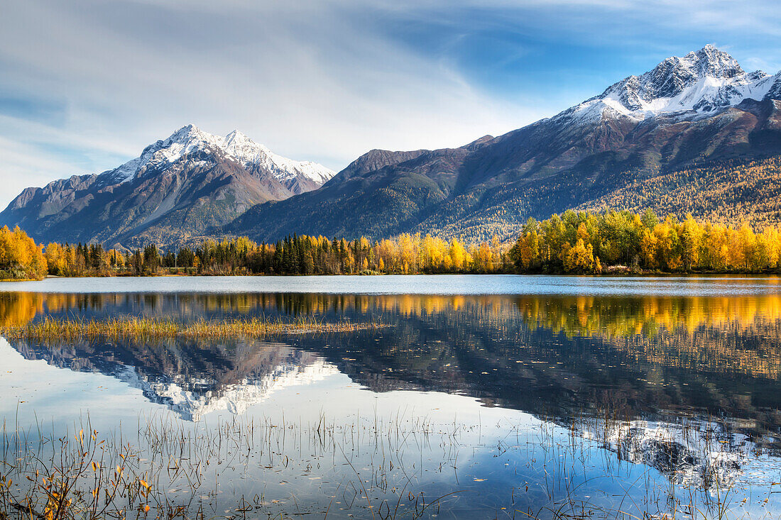 'The snowcapped Chugach Mountains and autumn foliage reflecting in Reflections Lake along the Glenn Highway in the Matanuska Susitna Valley; Alaska, United States of America'