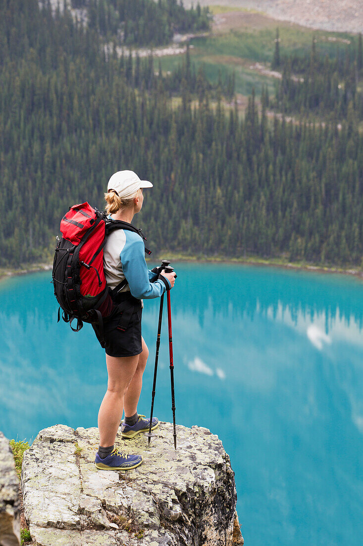 'Female hiker on rock cliff overlooking blue alpine lake; British Columbia, Canada'