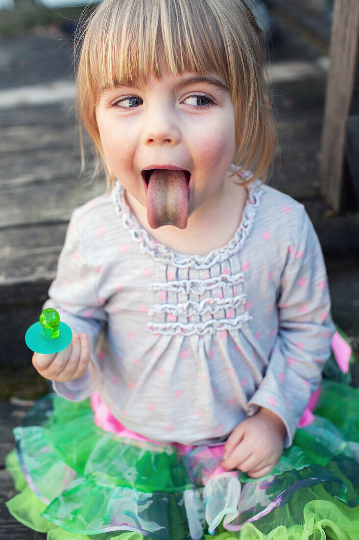 'Young girl sticking out tongue after sucking on green ring candy; Toronto, Ontario, Canada'