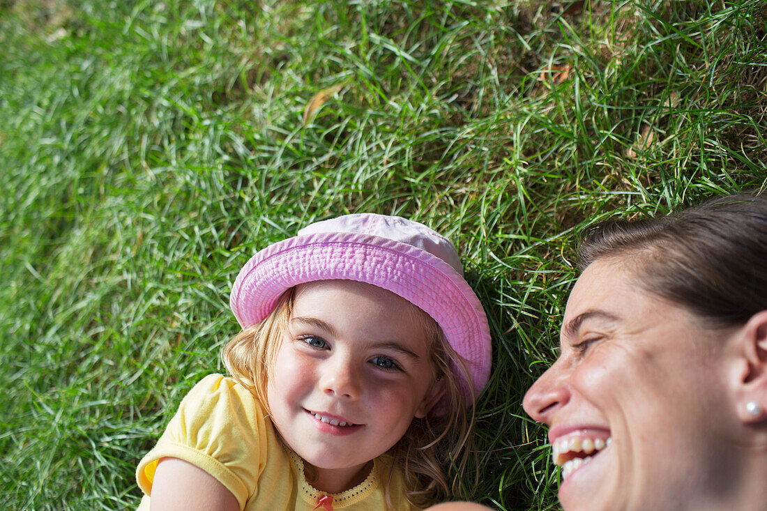 'Young girl laying on the grass with her mother laughing; Toronto, Ontario, Canada'