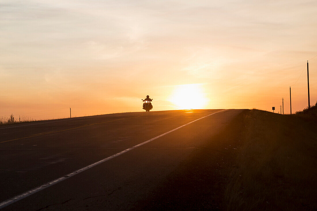 'Man on a motorcycle at twilight on a highway, near Edmonton; Alberta, Canada'