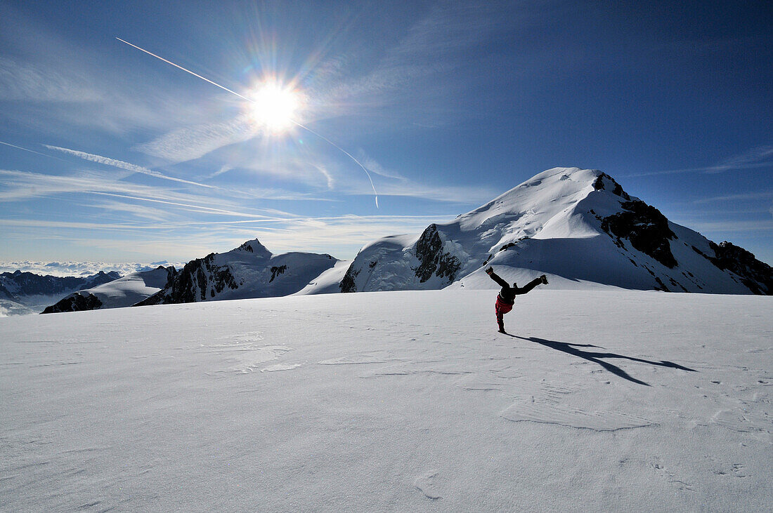 Bergsteiger macht einen Kopfstand am Gipfel des Dome de Gouter, Mont Blanc im Hintergrund, Mont Blanc Massiv, Frankreich