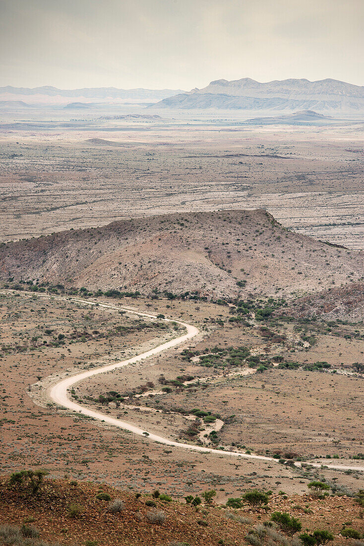 Kurvige staubige Straße im Hochland durch karges Gebiet, Namibia nahe Windhoek, Afrika