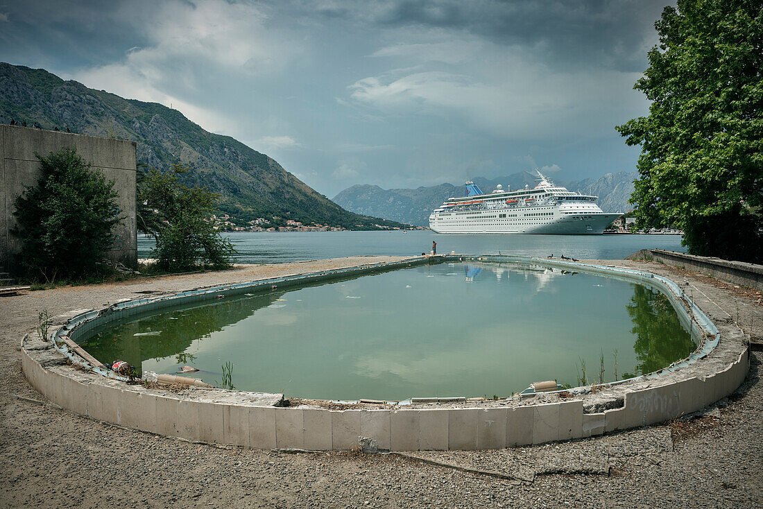 ein verlassenes marodes Hotel Schwimmbad vor Luxus Kreuzfahrt Schiff in der Bucht von Kotor, Adria Küste, Montenegro, Westlicher Balkan, Europa, Mittelmeer