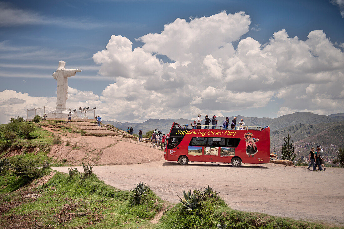 Red Tourist Bus stopping at the viewing platform of the white Christ Statue with view to the surrounding Andes Cuzco, Peru, South America