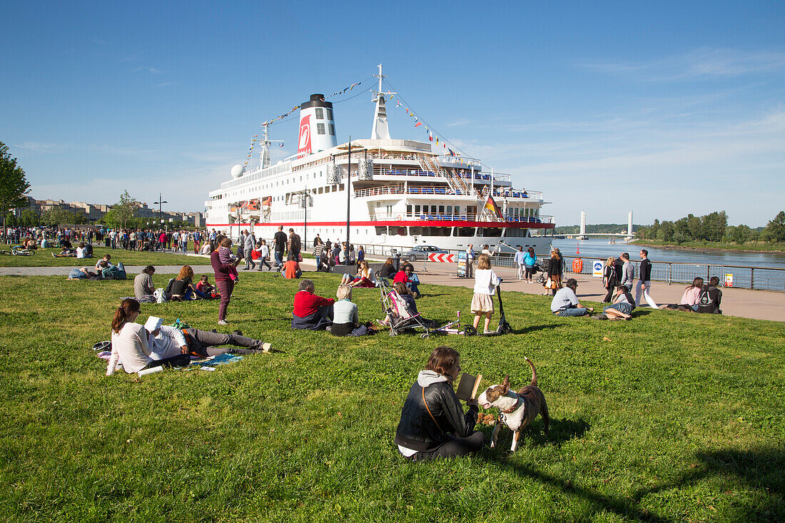 Menschen genießen einen sonnigen Sonntag im Park mit Kreuzfahrtschiff MS Deutschland (Reederei Peter Deilmann) am Ufer von Fluss Garonne, Bordeaux, Gironde, Aquitanien, Frankreich, Europa