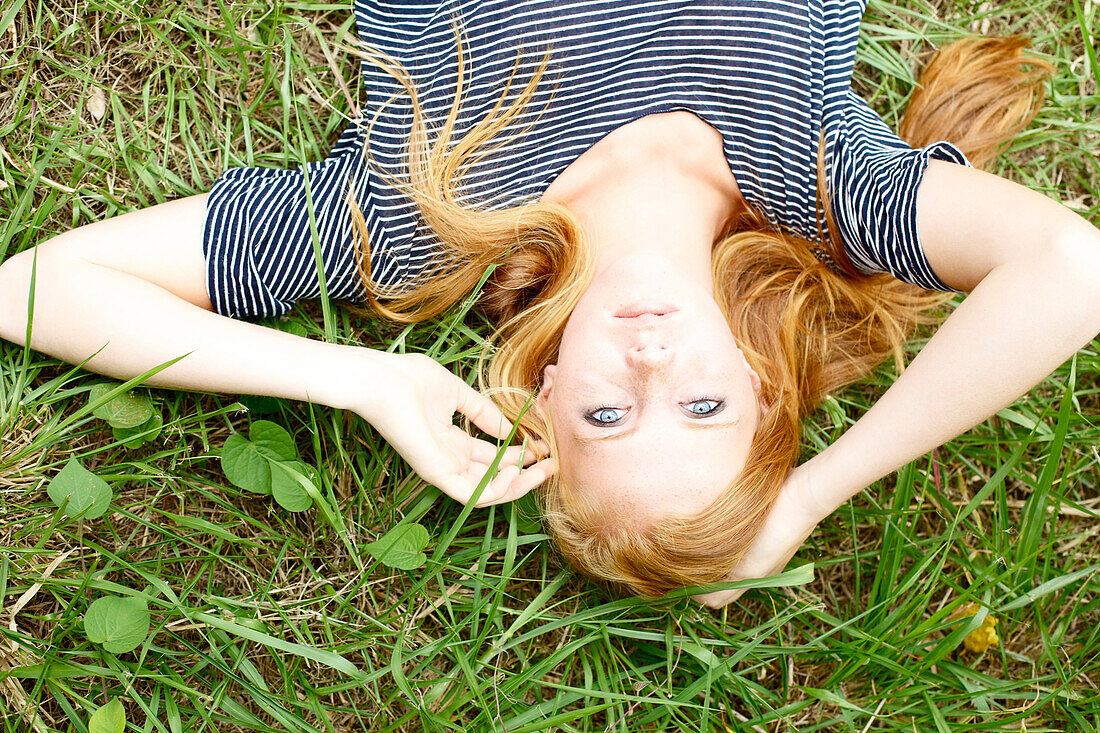 'A young woman with long red hair laying in the grass;Kauai hawaii united states of america'