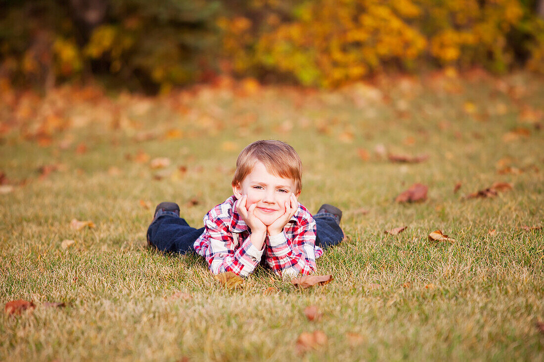 'Portrait of a young boy laying in the grass in a park in autumn;Edmonton, alberta, canada'