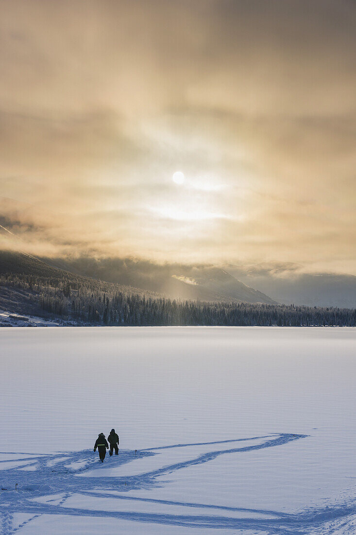 Sillhouetted Ice Fisherman On Summit Lake, Clouds Clearing From The Kenai Mountains Behind The Lake, Chugach National Forest, Backlit Sun, Winter, Southcentral Alaska, Usa.